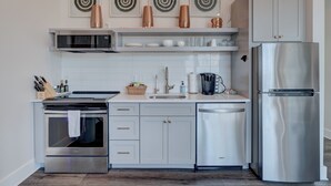 A modern kitchen with stainless steel appliances, white cabinetry, and decorative wall art. - The Hive 206 Sweeter (Wilmington)