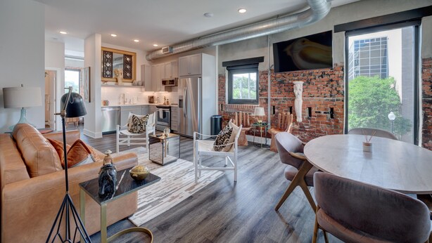 A modern living room with a leather sofa, a round dining table, and a kitchen in the background. - The Hive 207 Bees Knees by BlueStar (Wilmington)