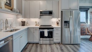A modern kitchen with stainless steel appliances, white cabinetry, and a built-in oven. - The Hive 207 Bees Knees by BlueStar (Wilmington)
