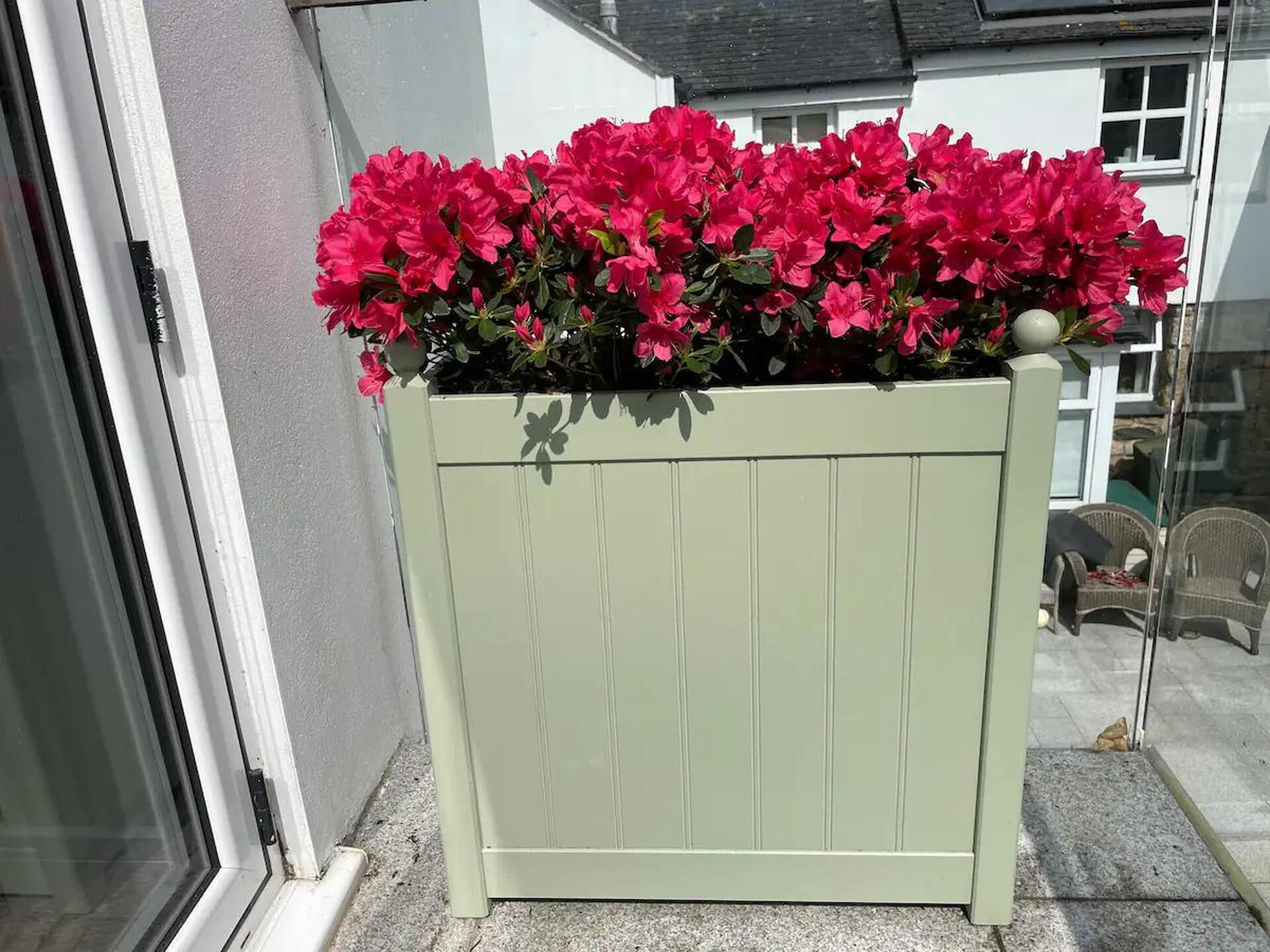 A light green wooden planter box with vibrant pink flowers on a balcony.