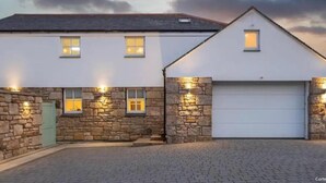 A two-story house with a stone facade, a garage, and a paved driveway. - Immaculate Studio Apartment Just Outside Penzance (Penzance)