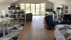 A spacious room with a high ceiling, a large window, a sofa, a desk, and a bookshelf. - Immaculate Studio Apartment Just Outside Penzance (Penzance)