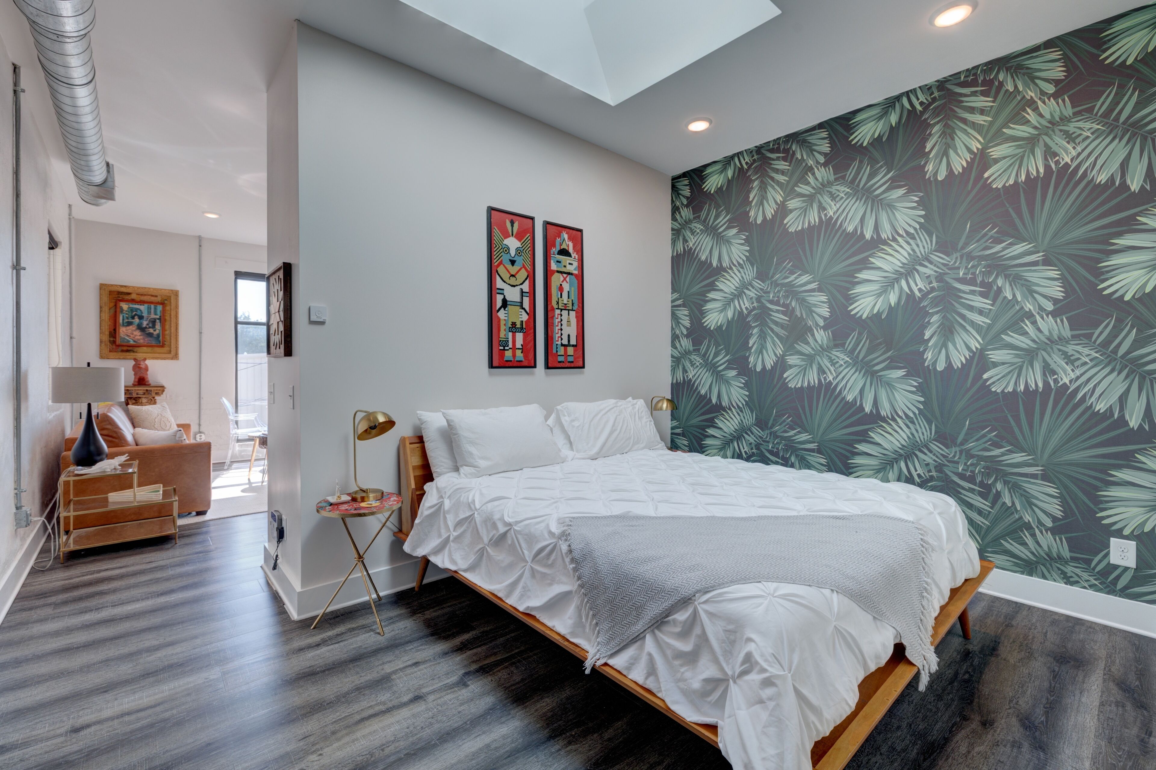 A bedroom with a bed, a nightstand, a lamp, a chair, and a wall with a tropical leaf pattern.