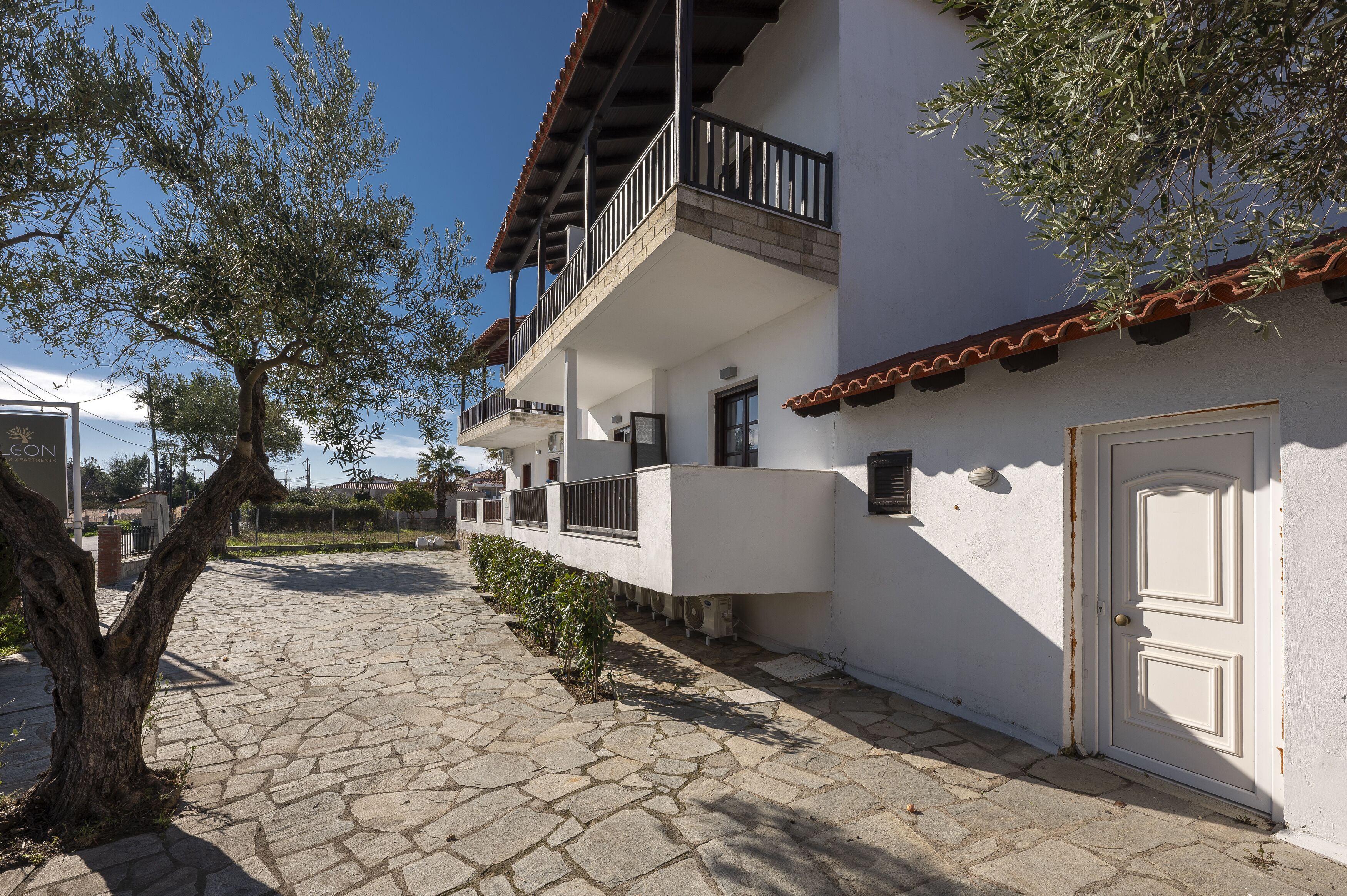 A white building with a balcony, a tiled courtyard, and a door.