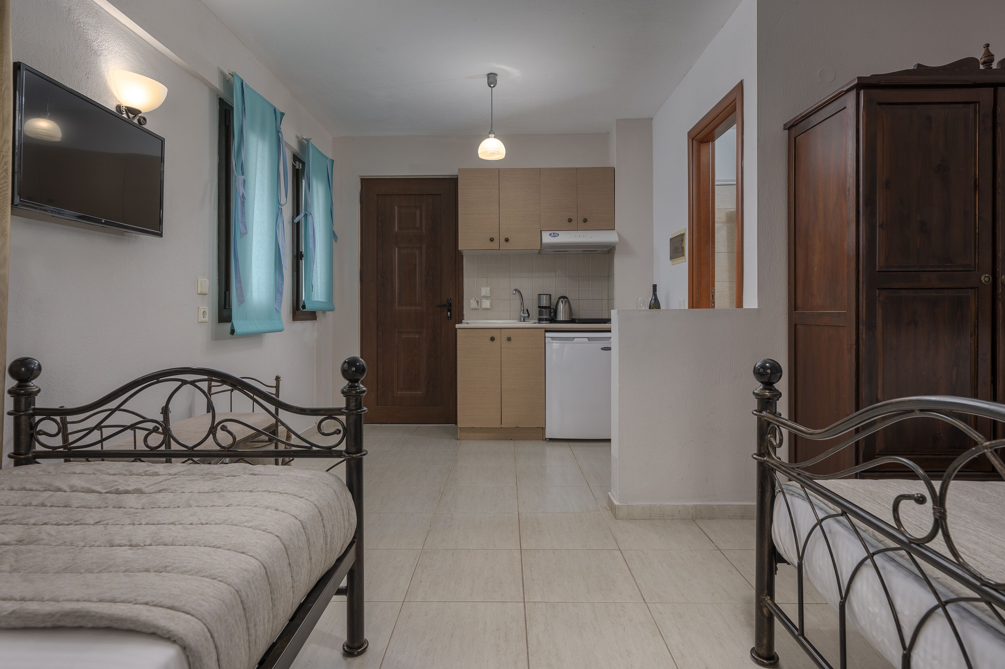 A bedroom with a bed, a TV, and a kitchenette in the background.