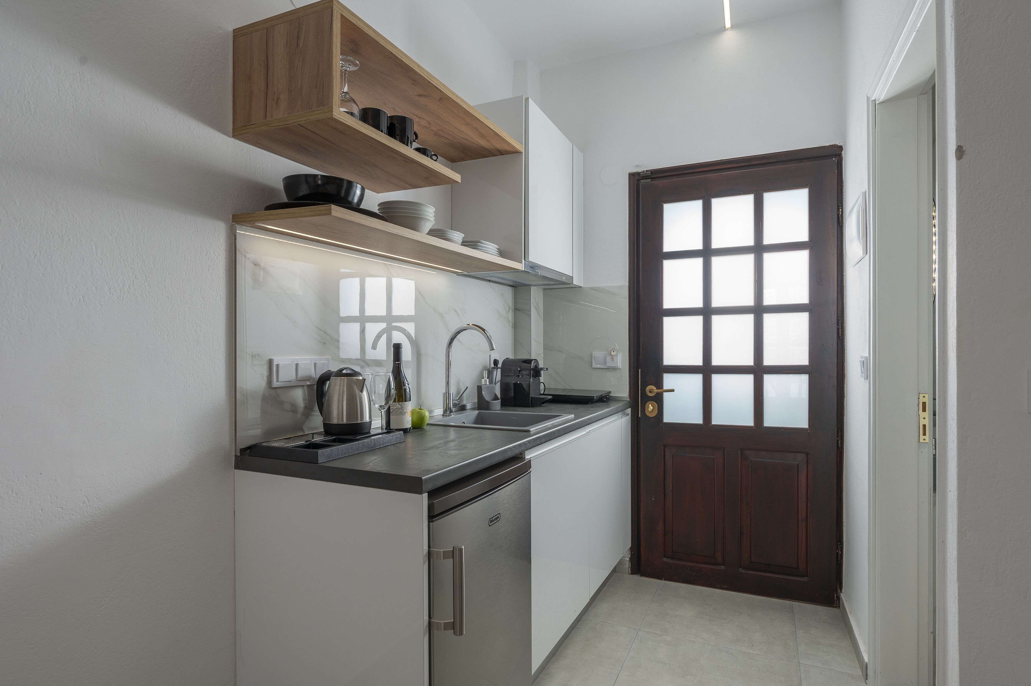 A compact kitchen with a built-in dishwasher, a coffee maker, and a kettle on the counter.