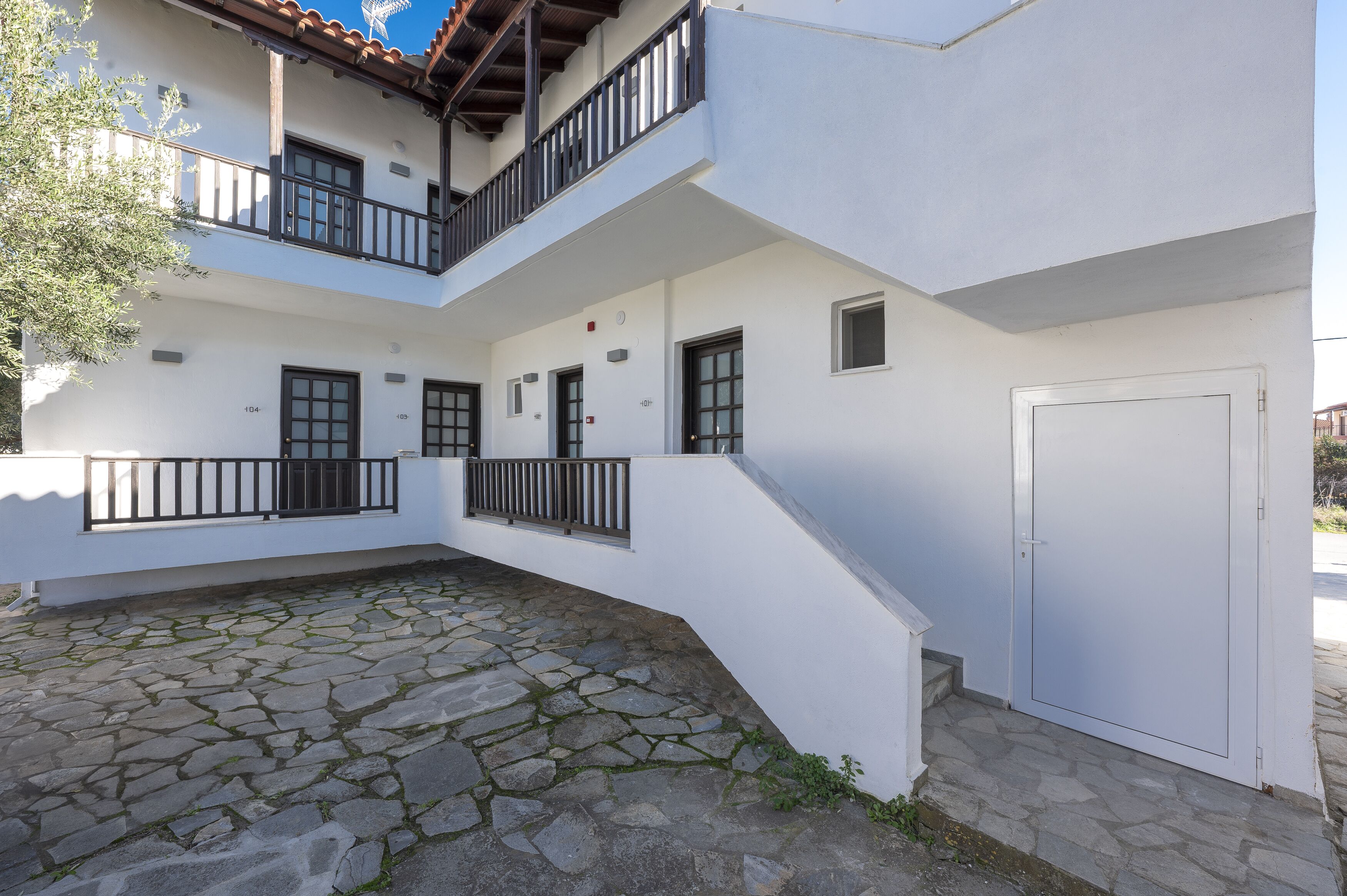 Un edificio de dos pisos con un patio de piedra, balcones y fachada blanca.