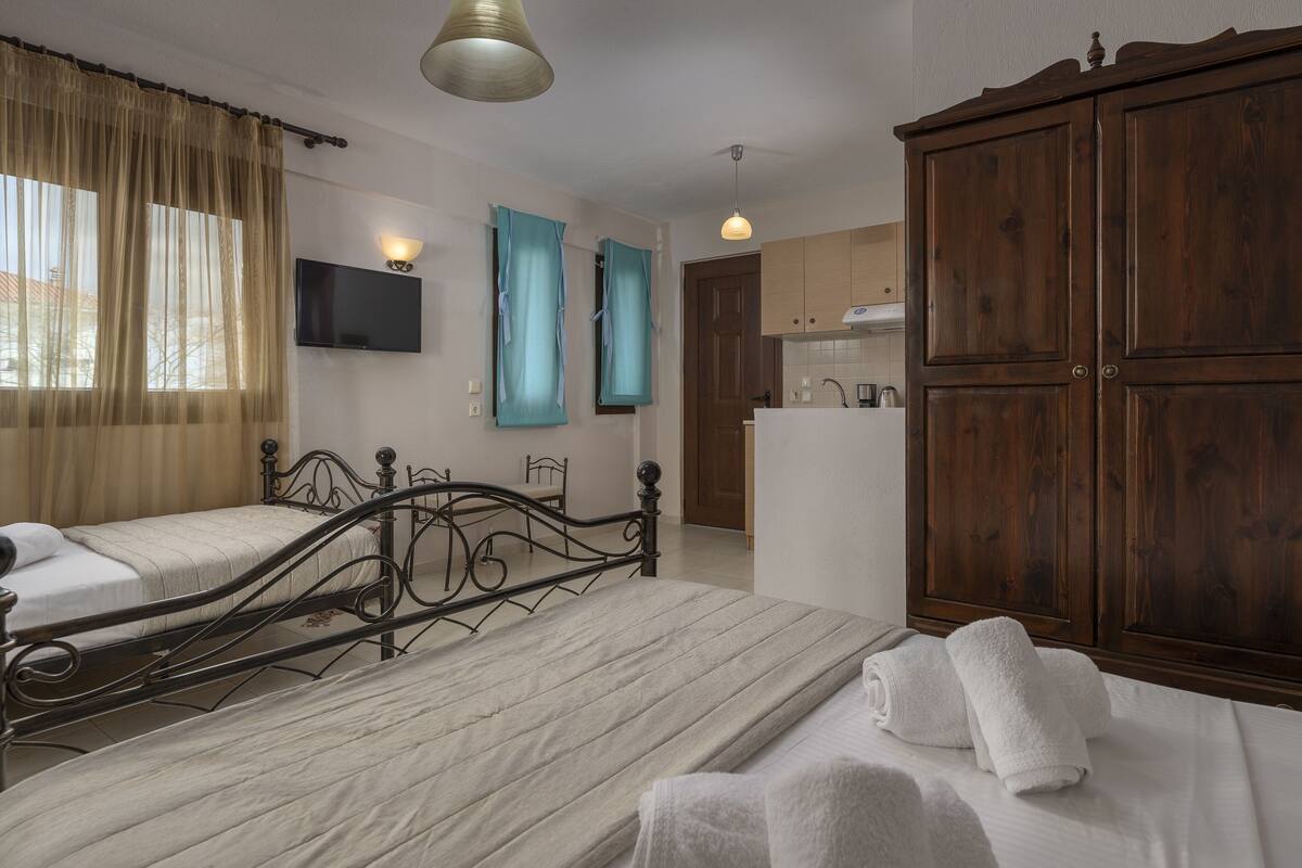 A hotel room with two beds, a wardrobe, a television, and a bathroom visible through an open door.