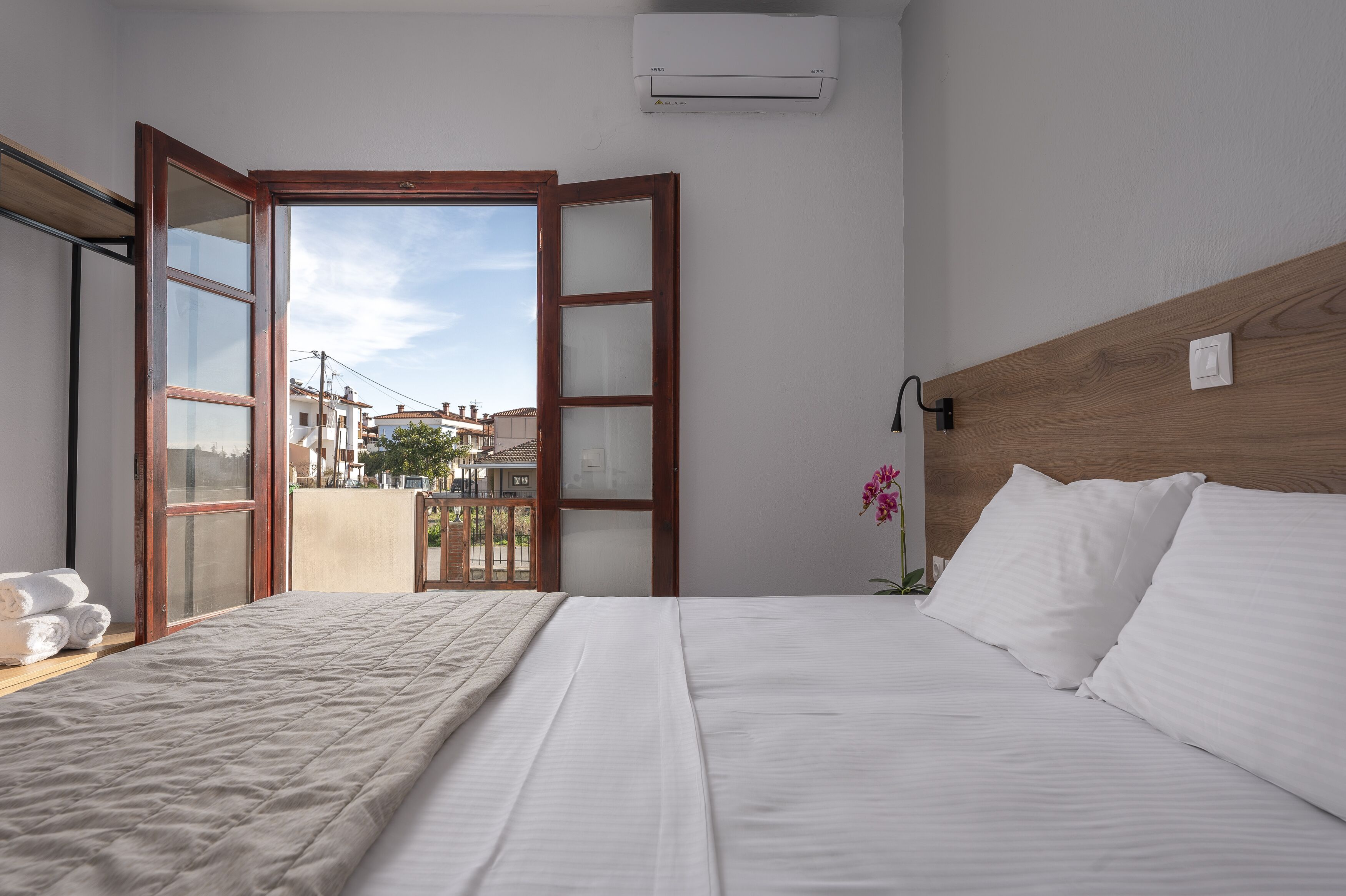 A hotel room with a bed, a wooden headboard, an open door leading to a balcony, and an air conditioning unit on the wall.