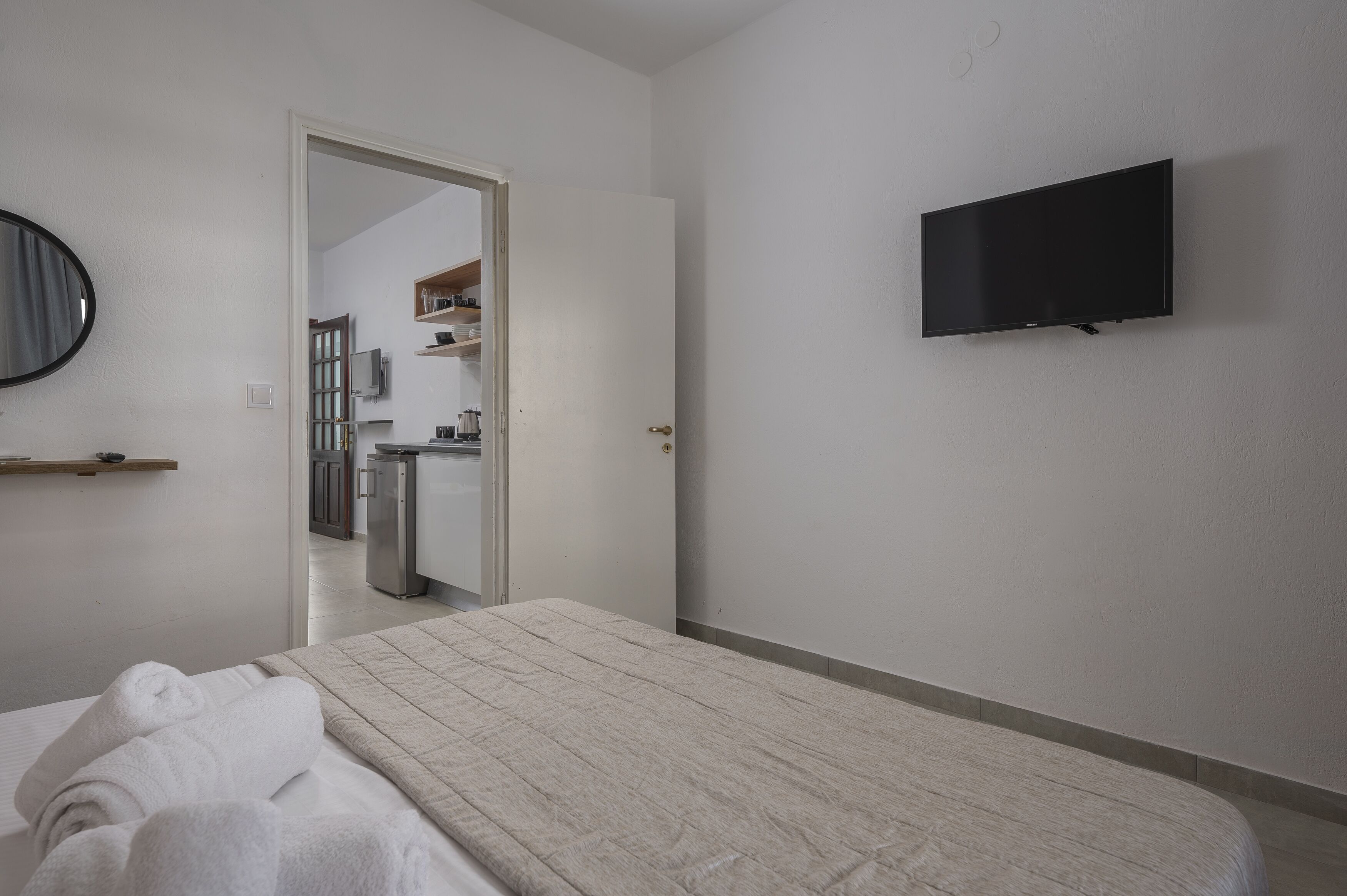 Une chambre d’hôtel avec un lit, un téléviseur fixé au mur et une salle de bain visible à travers une porte ouverte.