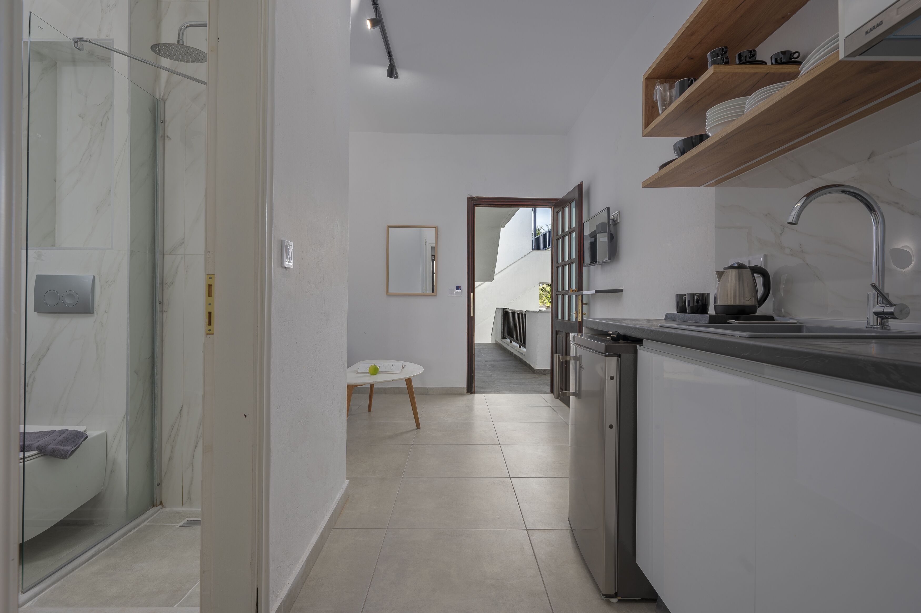 A modern kitchen with a built-in dishwasher, a sink with a kettle, and a wooden shelf above the counter.