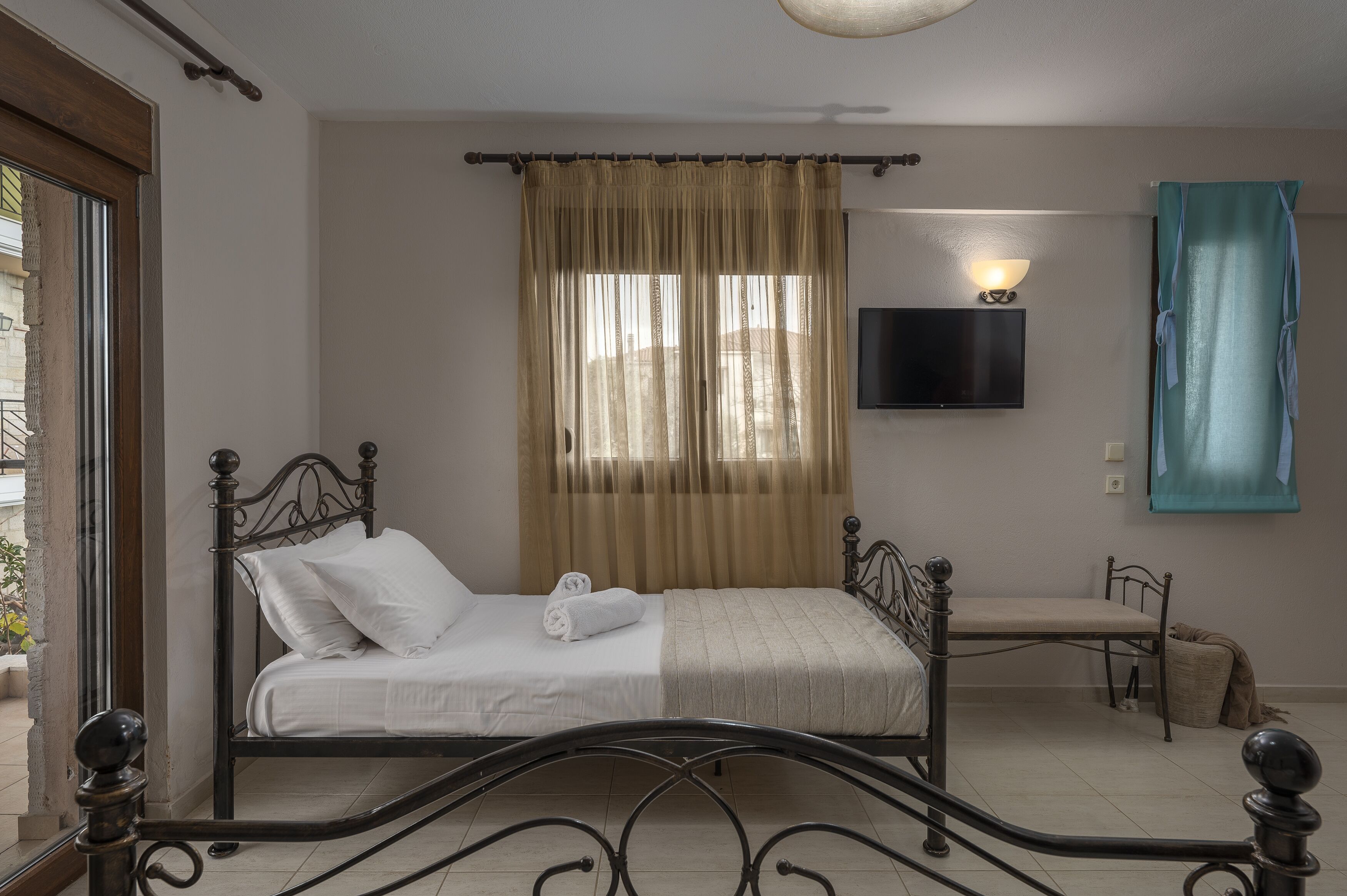 Une chambre à coucher avec un lit, un banc, une télévision et une fenêtre avec des rideaux.