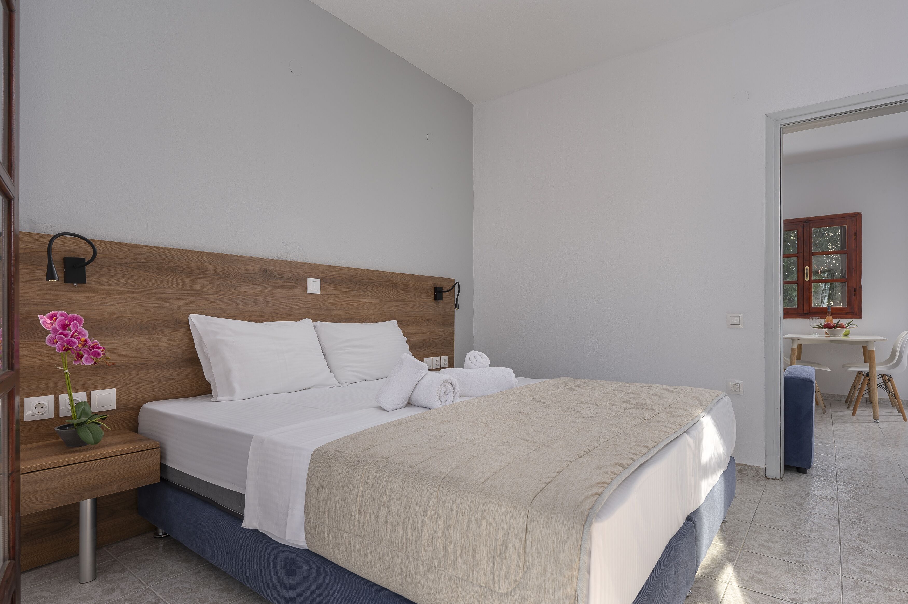 A bedroom with a wooden headboard, a bed with white linens, a bedside table with a lamp, and a small potted orchid.