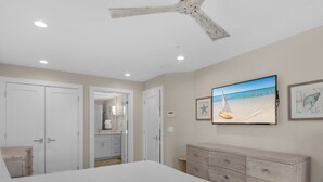 A bedroom with a bed, a dresser, a ceiling fan, and a TV displaying a beach scene. - Pet Friendly with Gulf Views! (Miramar Beach)