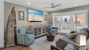 A living room with a large TV, a ceiling fan, and a view of the ocean through the windows. - Pet Friendly with Gulf Views! (Miramar Beach)