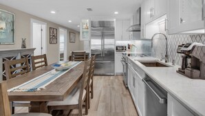 A modern kitchen with white cabinets, stainless steel appliances, and a wooden dining table with chairs. - Pet Friendly with Gulf Views! (Miramar Beach)