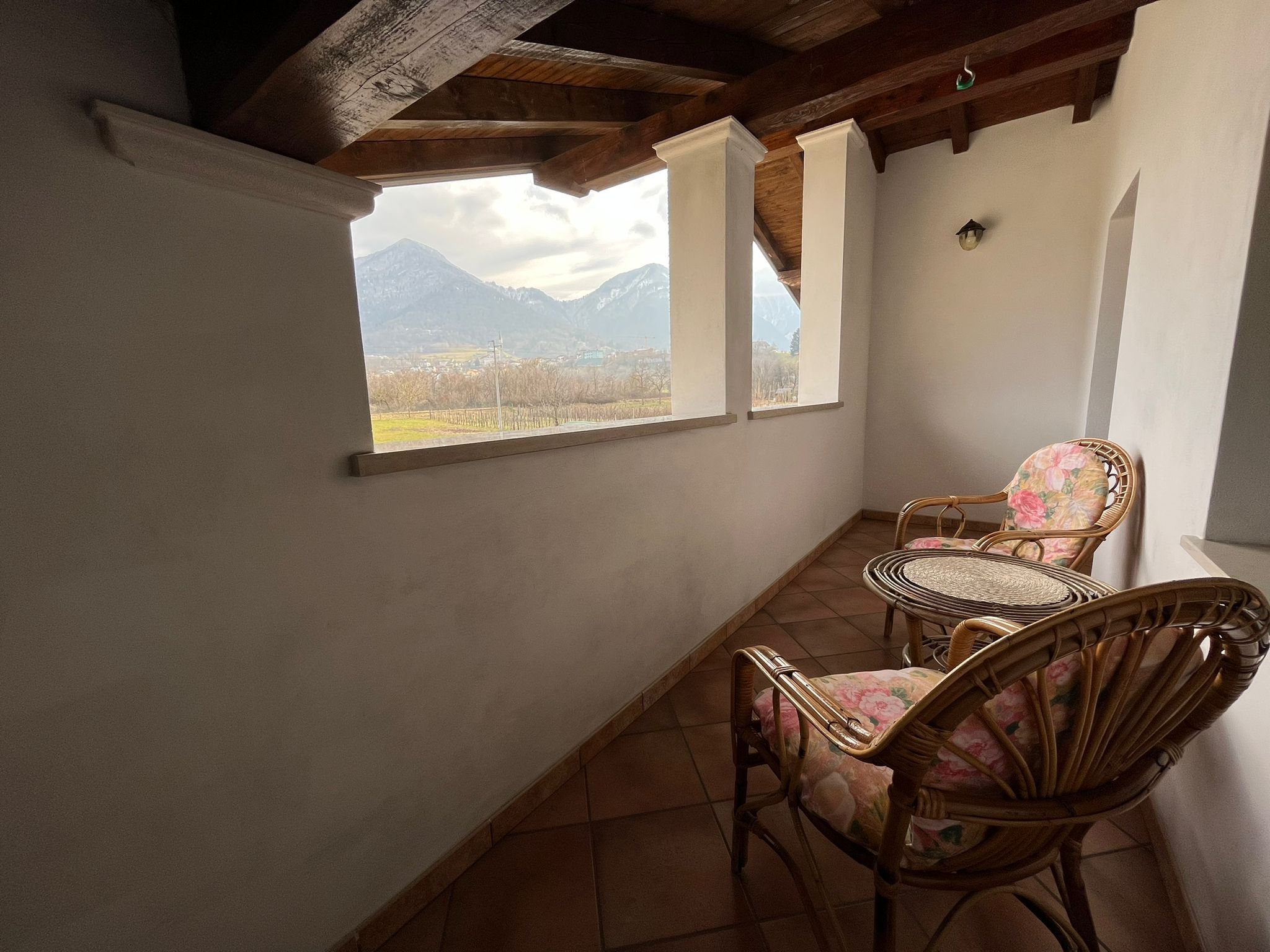 Un balcon avec deux fauteuils en osier et une petite table ronde, d’où l’on peut admirer un paysage montagneux.