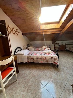 A room with a sloped ceiling, a bed with floral bedding, a chair, and a small table.