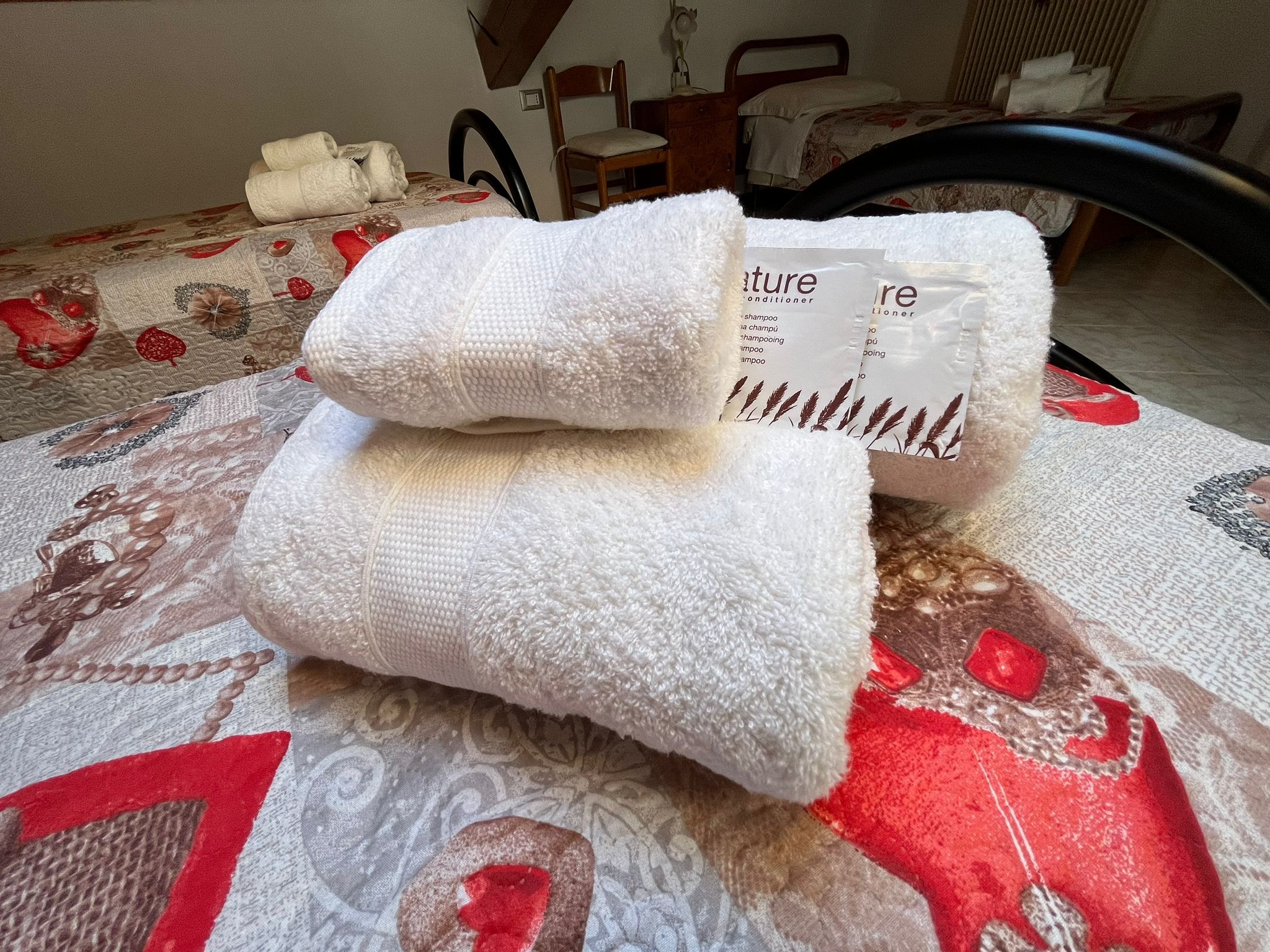 Un lit recouvert d’une couvre-lit à motifs et sur lequel sont posés deux serviettes enroulées.