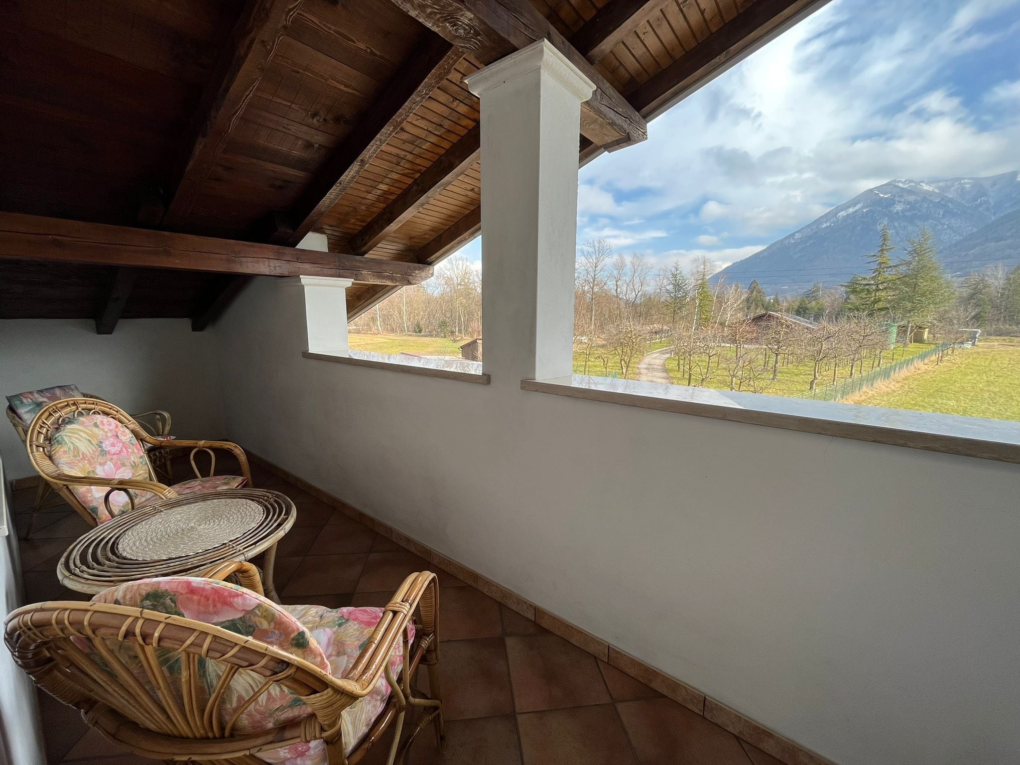 Une terrasse couverte, aménagée avec des meubles en osier, offrant une vue sur un paysage montagneux.