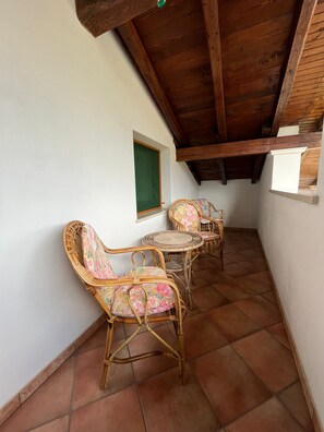 A covered patio area with wicker furniture and a tiled floor.