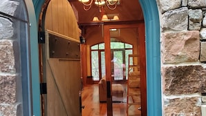 Un arc en pierre mène à un intérieur en bois, où l’on trouve un lustre et une porte.