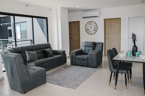 Ein modernes Wohnzimmer mit grauem Sofa, grauem Sessel und einem Esstisch mit Stühlen.