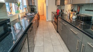 A modern kitchen with black countertops, stainless steel appliances, and a tiled floor. - Bay House (Bridlington)