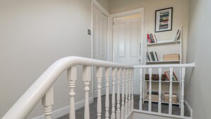 A staircase with white balusters leading to a landing with a bookshelf and a door. - Bay House (Bridlington)