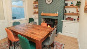 A dining room with a wooden table, four chairs, a fireplace, and shelves with books and decorative items. - Bay House (Bridlington)