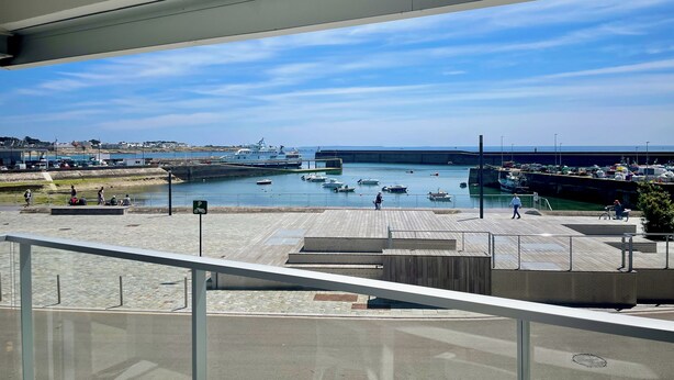 A view from a balcony overlooking a marina with boats, a pier, and a clear sky.