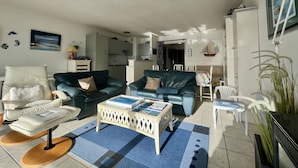A modern living room with a sofa, armchair, and coffee table. There is a kitchen in the background.