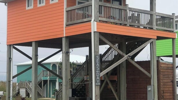 A two-story building with a balcony, wooden railings, and a sign that reads "SEASDAY." - Cozy studio walking distance to the beach, Seas the Day Beach House (Cameron)