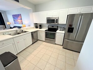 A modern kitchen with white cabinets, stainless steel appliances, a dishwasher, and a trash bin.