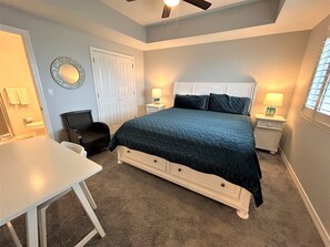 A bedroom with a bed, bedside tables, a chair, a desk, and a ceiling fan.
