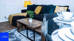 Un salon moderne avec un canapé, une table basse, une plante en pot et un coin repas avec une table mise pour deux personnes.