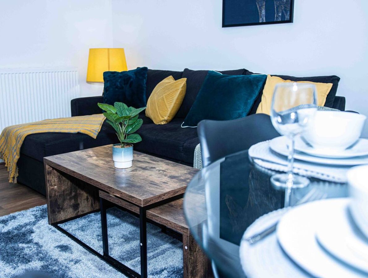 A modern living room with a sofa, a coffee table, a potted plant, and a dining area with a table set for two.