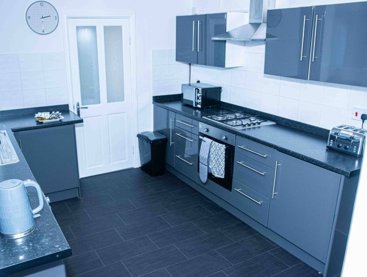 A modern kitchen with grey cabinets, a stove, a sink, and a clock on the wall.