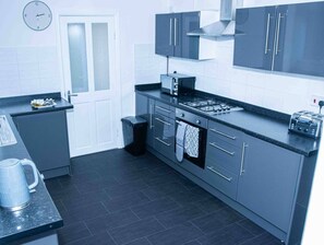 Een moderne keuken met grijze kastjes, een fornuis, een spoelbak en een klok aan de muur.
