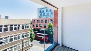 A view from a balcony overlooking a school building, a red bus, and a modern building with glass windows. - Impeccable 1-bed Apartment in London (London)