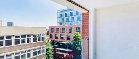 A view from a balcony overlooking a school building, a red bus, and a modern building with glass windows.