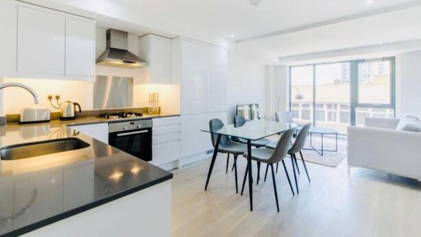 A modern kitchen with white cabinets, a black countertop, and a dining area with a glass table and chairs. - Impeccable 1-bed Apartment in London (London)