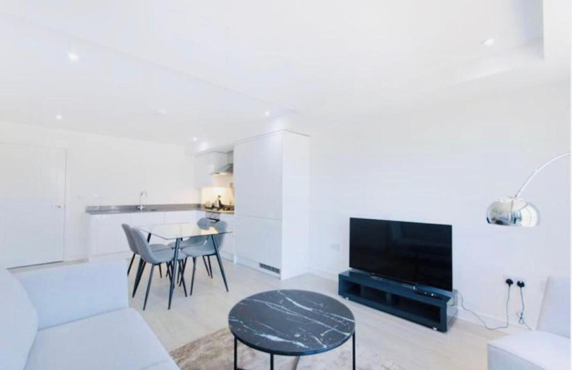 A modern living room with a flat-screen TV, a marble coffee table, and a dining area with chairs and a table.