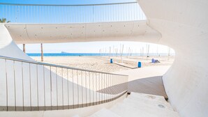 Una estructura arquitectónica moderna con diseño curvo, barandilla de metal y vistas a una playa y el océano.