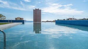 Una piscina con agua azul cristalina, rodeada por un muro bajo y un edificio alto al fondo.