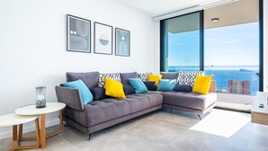 Una sala de estar moderna con un sofá seccional gris, una mesita redonda y un ventanal con vistas al mar.