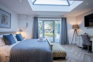 A bedroom with a skylight, a bed with blue bedding, a desk, and a TV.