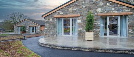 A stone building with large glass doors and windows, a covered patio, and a landscaped driveway.