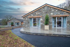 A stone building with large glass doors and windows, a covered patio, and a landscaped driveway.