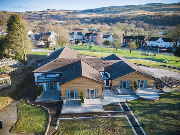 A modern two-story house with a sloped roof, a covered patio, and a landscaped front yard.